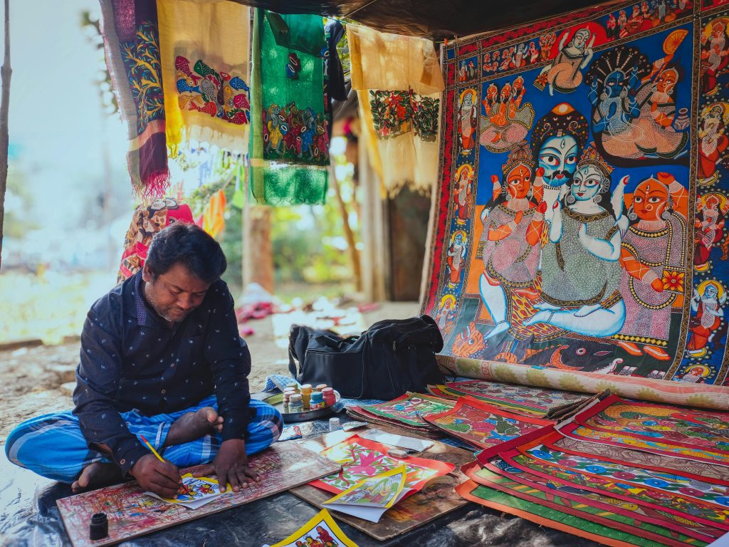 An Indian artist skillfully creating vibrant Pattachitra paintings outdoors in Midnapore, India.